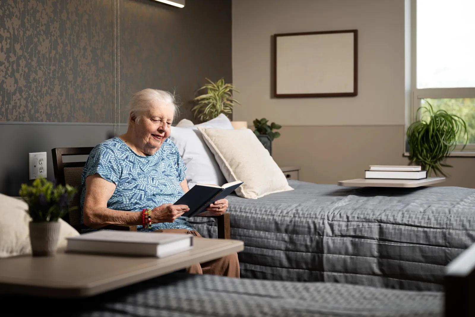 Resident reading a book beside her bed in a newly renovated room